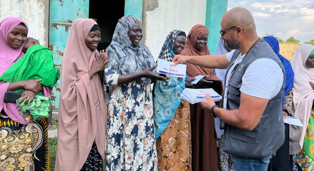Man distributing Zakat envelopes to women in Africa.