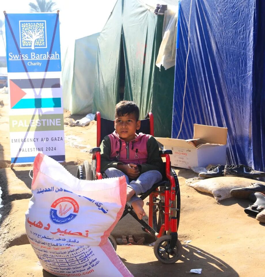 A child in a wheelchair sits next to a large bag of flour for Zakat al-Fitr distribution in Gaza.