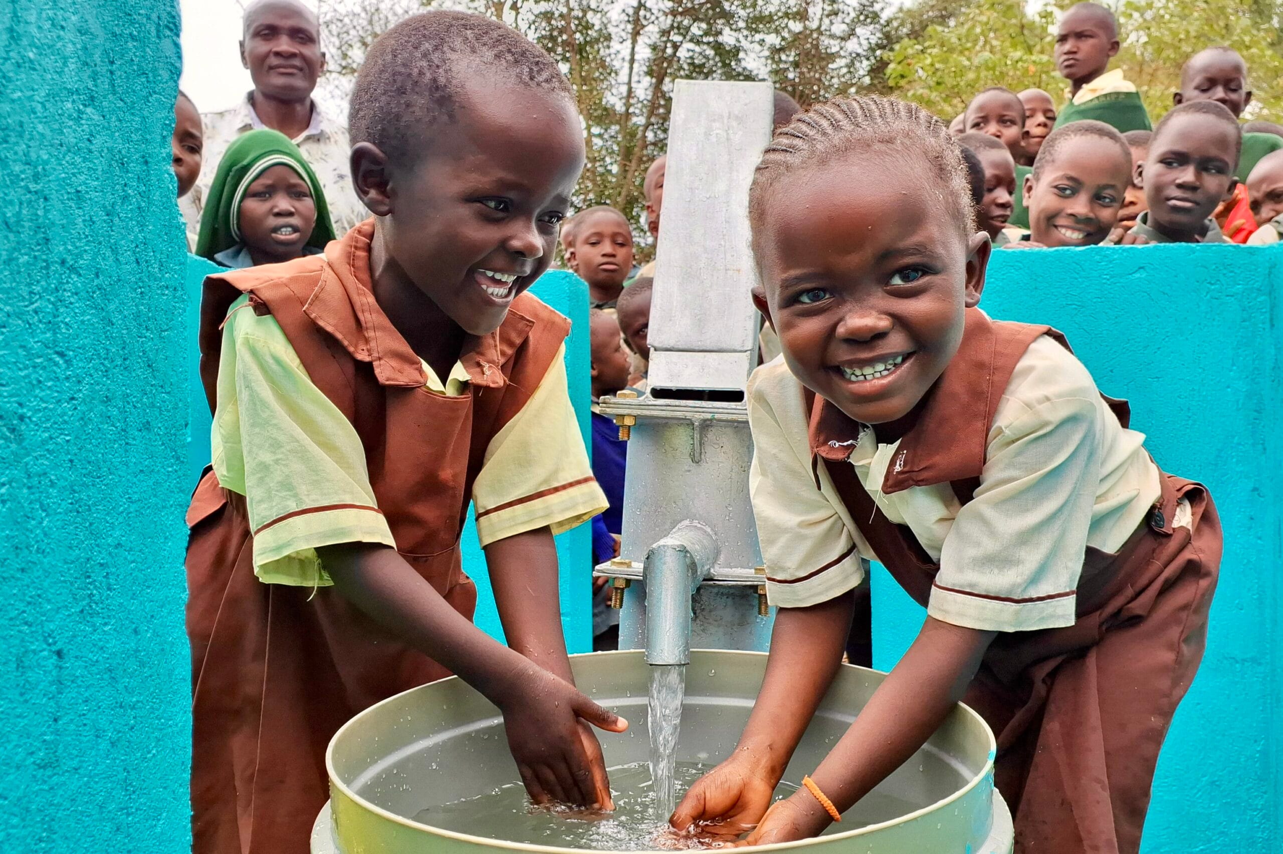 Happy African children playing with clean water next to a new community water well.