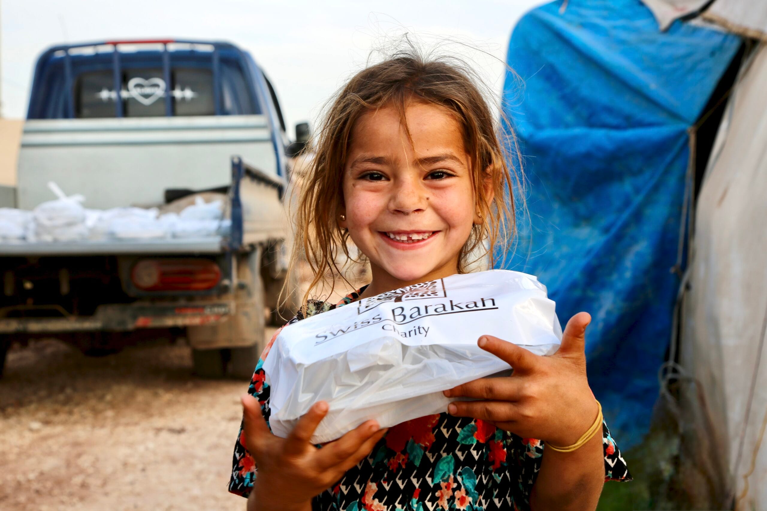 Smiling girl holding a warm Iftar meal during a charity food distribution project.