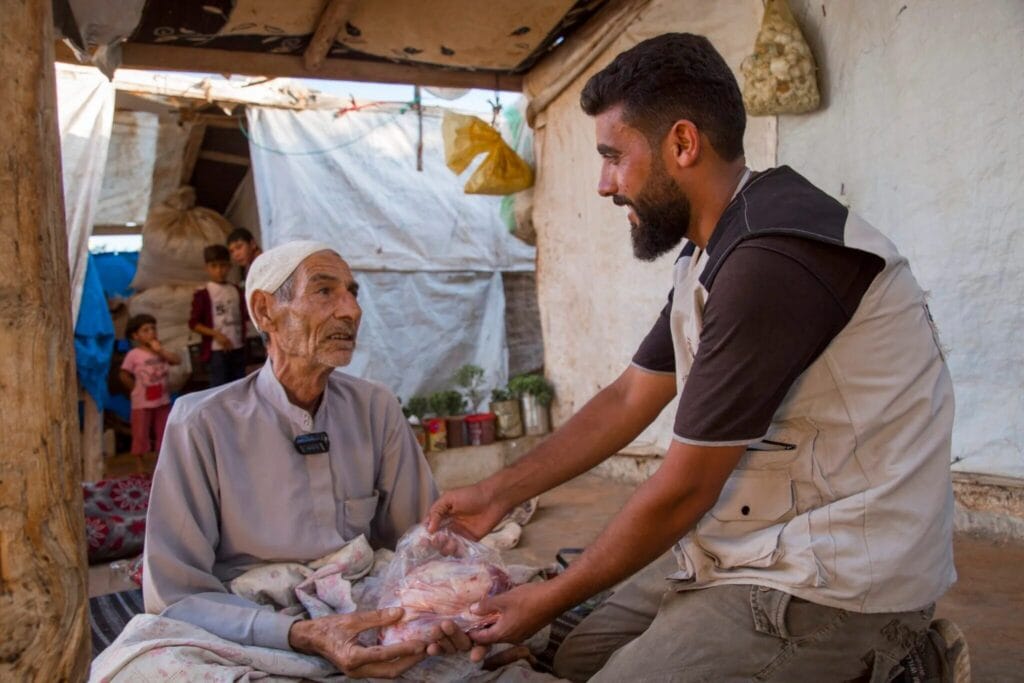 An aid worker distributing fresh meat from qurban donations to elderly people in need.