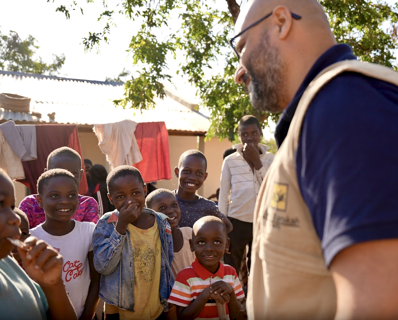 A smiling humanitarian worker from the Barakah charity interacts with a group of orphan children in an African village.